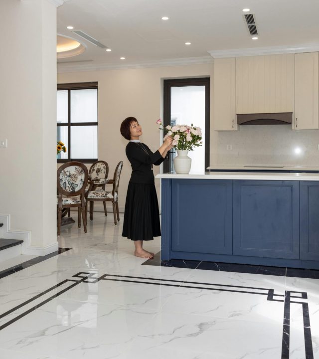 Elegant open-plan kitchen with a woman arranging flowers adds a homely touch.